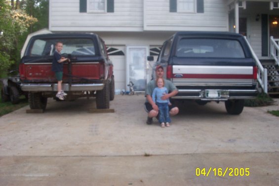 Two Ford Broncos parked in a driveway, one red and black, the other blue and black