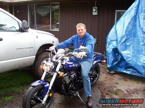 Blue motorcycle with chrome accents, ridden by a man in a blue hoodie, parked next to a silver Dodge Ram 3500 truck