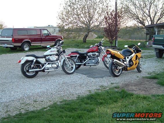 Three motorcycles parked on gravel with a pickup truck in the background
