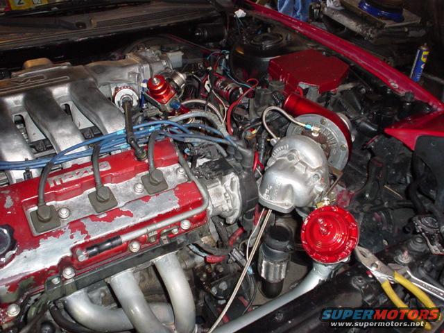 Engine bay with turbocharger, intercooler piping, and red blow-off valve. Wires and hoses are visible