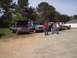 1989 Ford Bronco - Several trucks and SUVs are parked in a gravel lot on a sunny day.