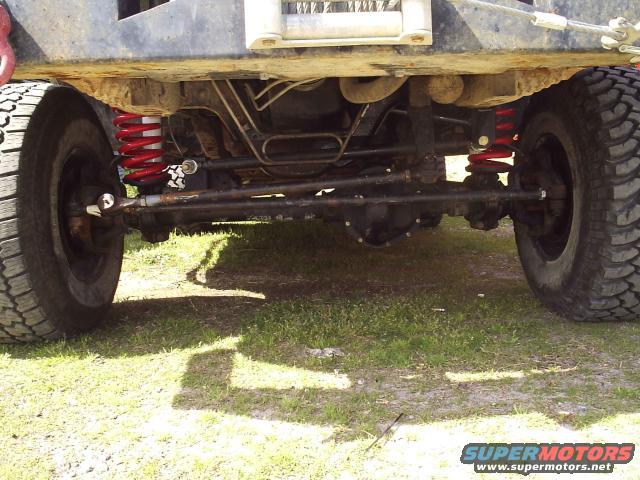 Undercarriage of a modified off-road vehicle with red springs, large tires, and visible suspension components