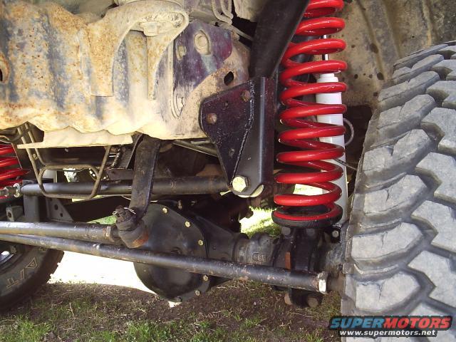 Close-up of red coil spring and shock absorber on a vehicle's front axle with large tire tread visible
