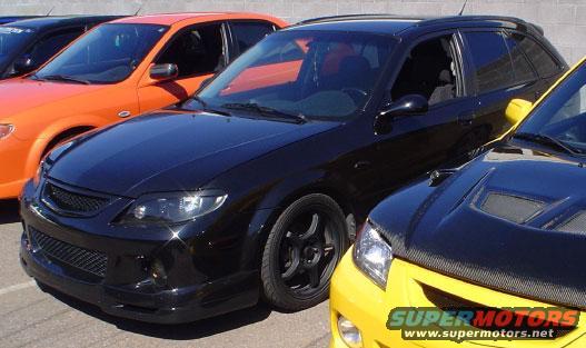 Black wagon with aftermarket wheels and body kit, parked next to an orange car and a yellow car