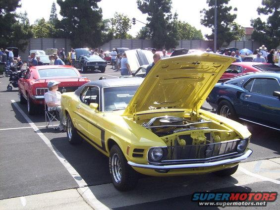 Yellow 1970 Ford Mustang with hood open, parked at a car show