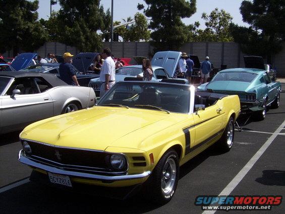 Yellow 1970 Ford Mustang convertible with black side stripes parked at a car show