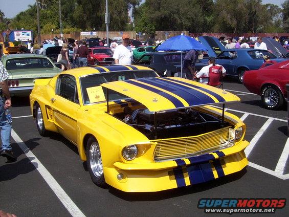 Yellow custom car with blue stripes, hood open, parked at an outdoor car show