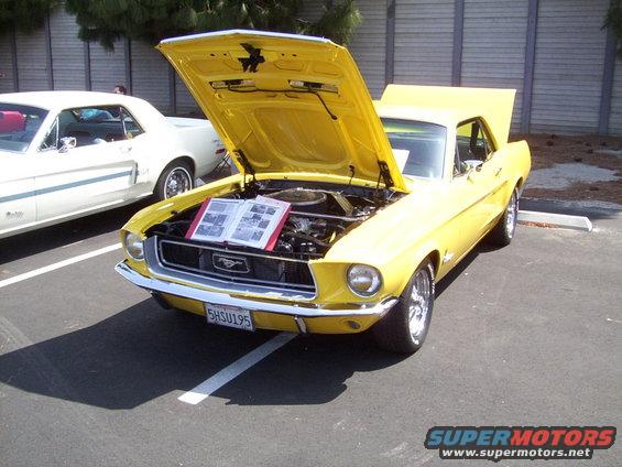 Yellow 1967 Ford Mustang, hood open, showing engine and display book