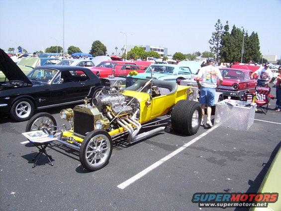 Yellow hot rod with large rear tires, exposed V8 engine, and chrome accents