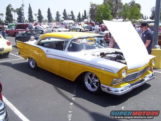 Two-tone yellow and white 1957 Ford Fairlane 500 with hood open, parked at an outdoor car show