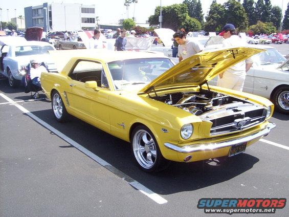 Yellow 1965 Ford Mustang coupe with hood open, chrome wheels, parked in a lot