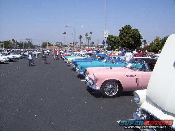 Row of classic Thunderbirds, including a pink one, parked at an outdoor car show