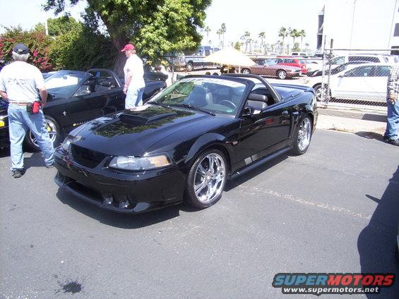 Black convertible Mustang with a hood scoop and chrome wheels parked outside