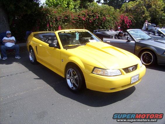 Yellow convertible Mustang with a hood scoop and chrome wheels parked on asphalt