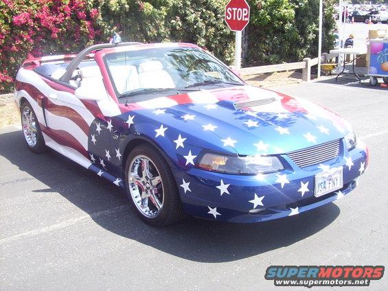 2002 Ford Mustang convertible painted with American flag graphics, chrome wheels, and a scoop on the hood. License plate reads JSA FNY