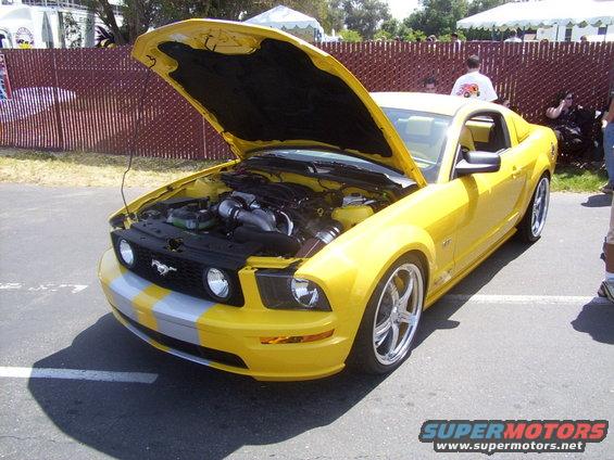 Yellow Ford Mustang with hood open, showing engine and custom wheels