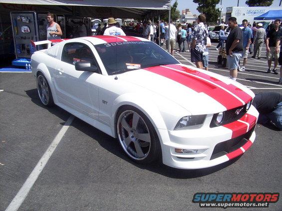 White Ford Mustang GT with red stripes on hood and roof. Custom body kit and wheels