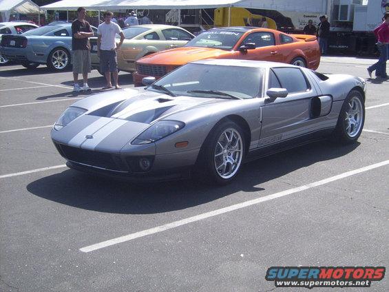 Silver Ford GT with dual gray racing stripes, parked in a lot