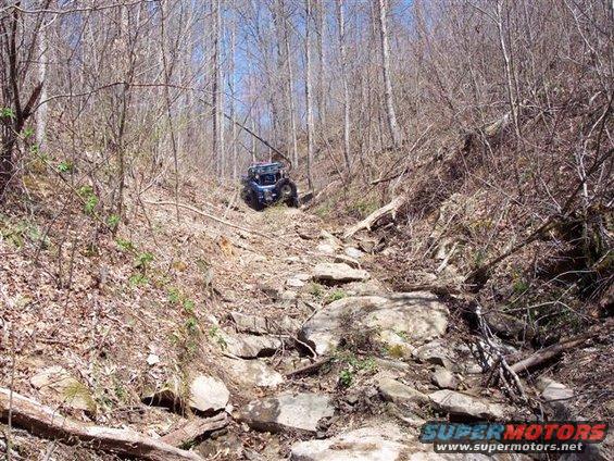 Side-by-side UTV navigating a steep, rocky trail through a wooded area