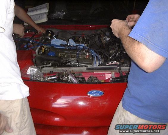 1994 Ford Probe engine bay with people working on it. Blue spark plug wires visible