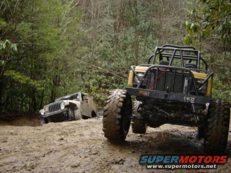 Two off-road vehicles stuck in mud on a trail, one in the foreground and another in the background