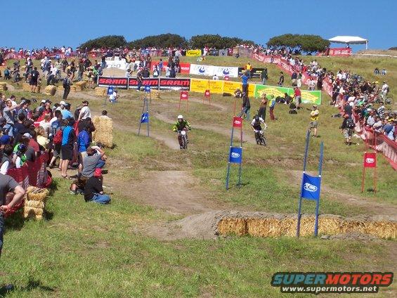 Dirt track race with spectators and hay bales, cyclists in motion