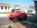 1989 Jeep YJ - A red Jeep Wrangler is parked on the side of a street in front of houses.
