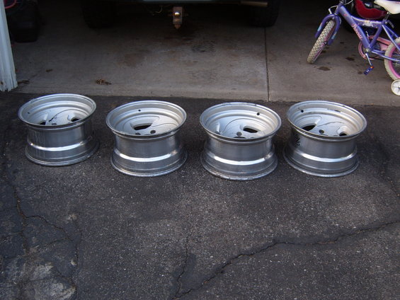 Four silver aluminum alloy wheels with five lug holes and a multi-spoke design, resting on asphalt