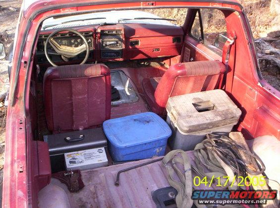 Interior of a red pickup truck with red seats, dashboard, and cargo area holding toolboxes and straps. A date stamp reads 04/17/2005