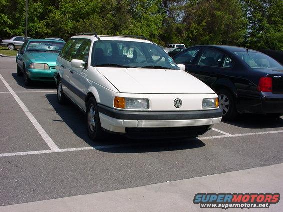 White station wagon parked in a lot, front view. Green car to the left, black sedan to the right. Paper on windshield says 4418