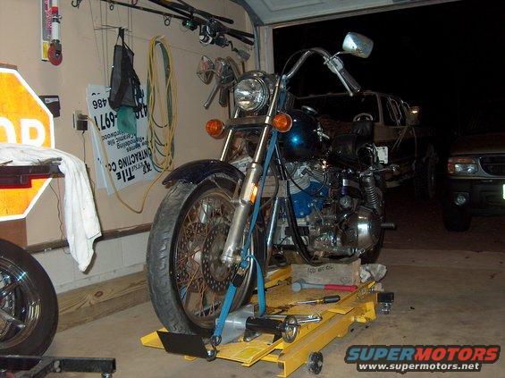 Blue motorcycle on a yellow lift, with a truck in the background