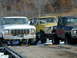 1979 Ford F-150 - Three lifted pickup trucks are parked on a trailer, with the front of a 1979 Ford F-150 prominently displayed.