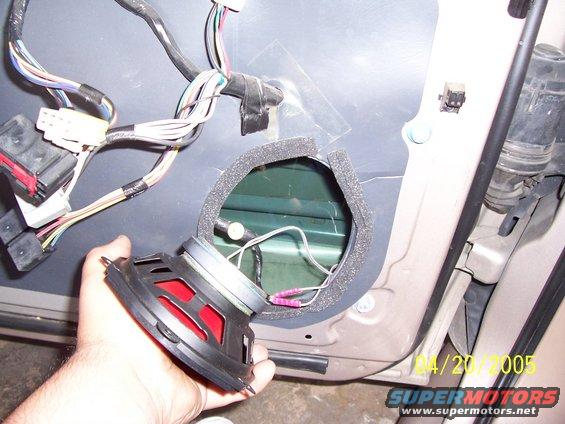 Car door panel removed, showing wiring harness and speaker removed from its mounting hole