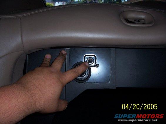 Hand pressing a button on a car's center console, showing a power outlet and a small button