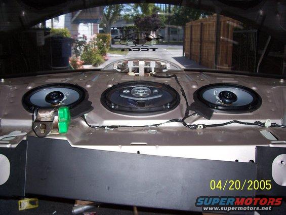 Rear speaker deck with three speakers installed, wires visible. Exterior scene visible through rear window