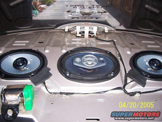 Car's rear deck with three speakers and wiring exposed. A green seatbelt buckle is visible