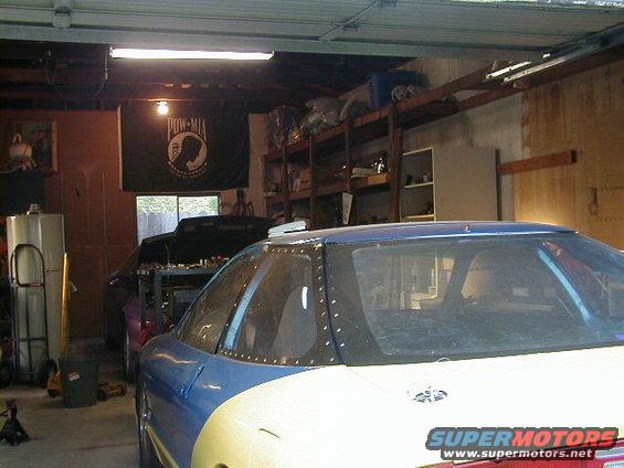 Cars in a garage, one is blue and white, the other is purple with hood up