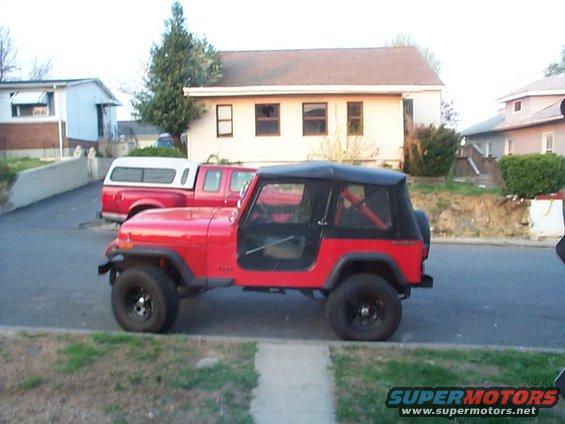 Red Jeep CJ parked on street next to a red pickup truck with a camper shell
