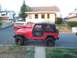 1989 Jeep YJ - A red Jeep CJ is parked on the street, with a red pickup truck and camper shell behind it.