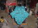 1969 Ford Bronco - A turquoise V8 engine is mounted on an engine stand in a garage, surrounded by tools and equipment.