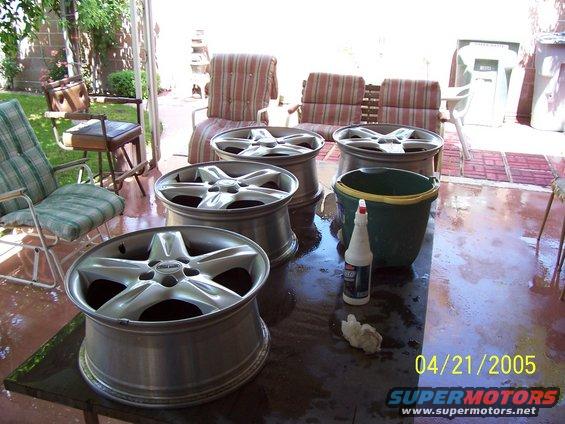 Four aluminum alloy wheels and cleaning supplies on a table outdoors