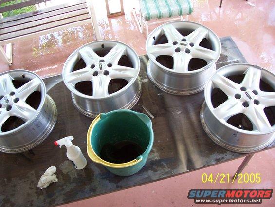 Four aluminum alloy wheels, a green bucket, and a spray bottle on a table