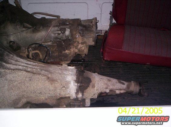 Two dirty transmissions and a red car seat are in the back of a vehicle