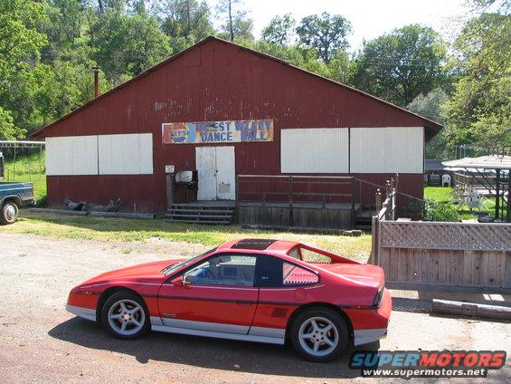 Red Pontiac Fiero GT parked in front of a red building with a sign that says 'Forest Wild Dance Hall'