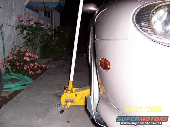 Car jack lifting the front fender of a light-colored car. Date stamp reads 04/21/2005