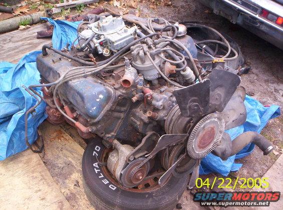 V8 engine with carburetor and fan, sitting on a tire and blue tarp