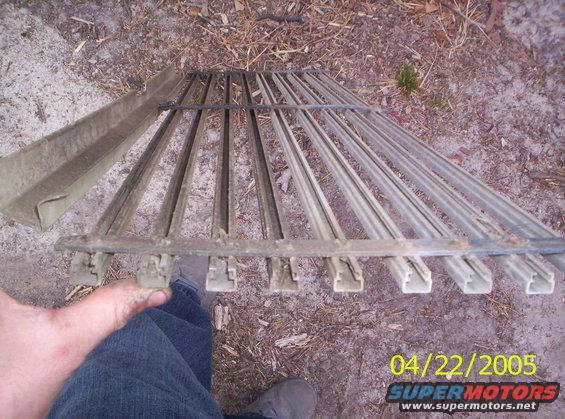Metal car grille with vertical bars and a separate channel piece lying on the ground
