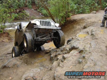Green Jeep Wrangler TJ navigating a rocky, muddy trail with a river nearby