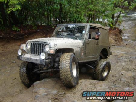 Mud-covered Jeep Wrangler TJ on a dirt trail with trees in the background