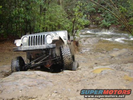 Jeep Wrangler navigating a muddy trail next to a stream